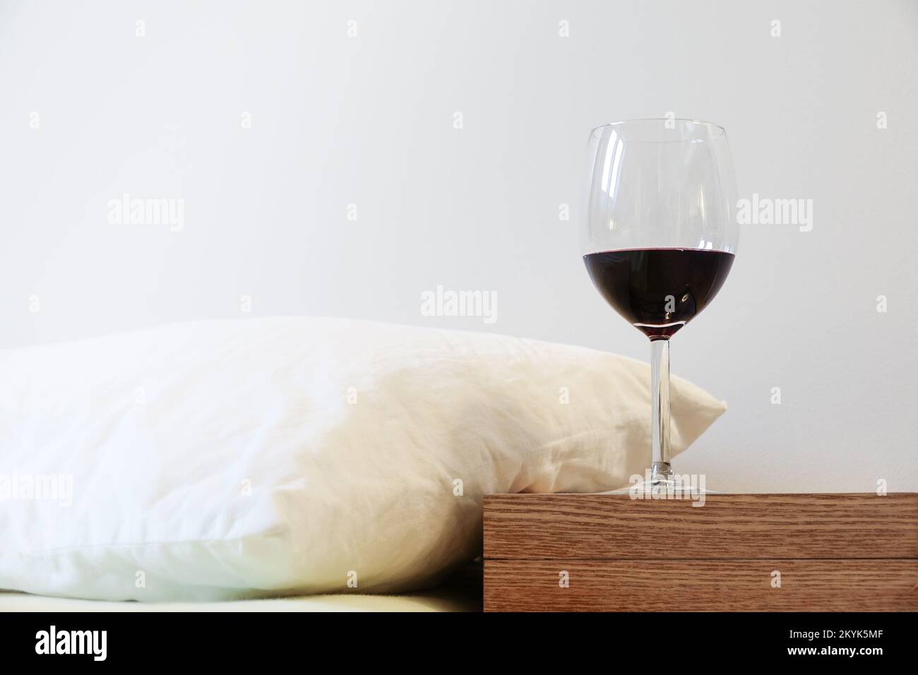 Cuscino e bicchiere di vino sul comodino. Concetto di abuso di alcool e problemi di sonno Foto Stock