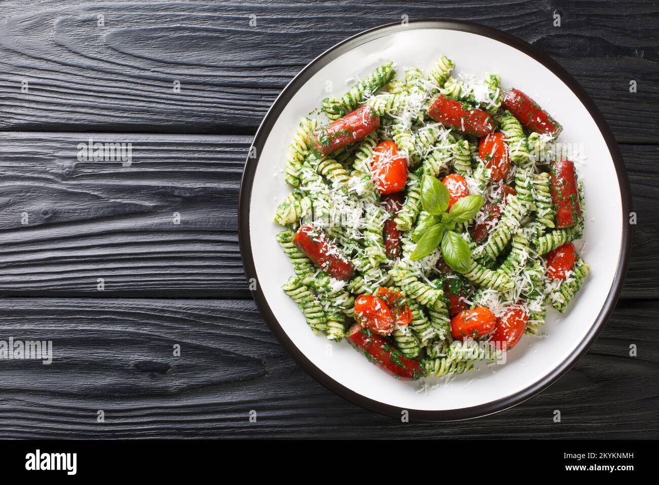 Salsiccia di Pesto verde Pasta con pomodori e parmigiano primo piano sul piatto della tavola. Vista orizzontale dall'alto Foto Stock