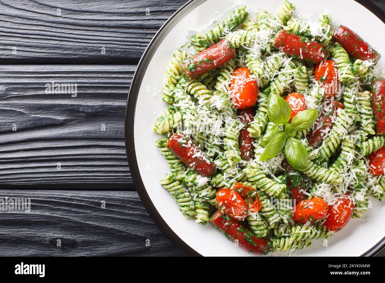 Insalata italiana di fusilli con salsicce, pomodori, pesto e parmigiano primo piano in un piatto sul tavolo. Vista orizzontale dall'alto Foto Stock