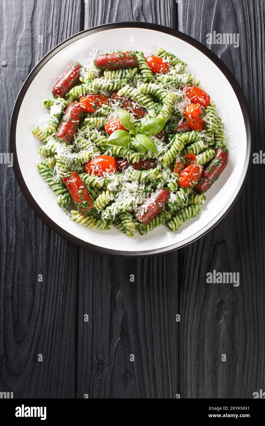 Fusilli con salsicce, pomodori, pesto e parmigiano in un piatto sul tavolo. Vista verticale dall'alto Foto Stock