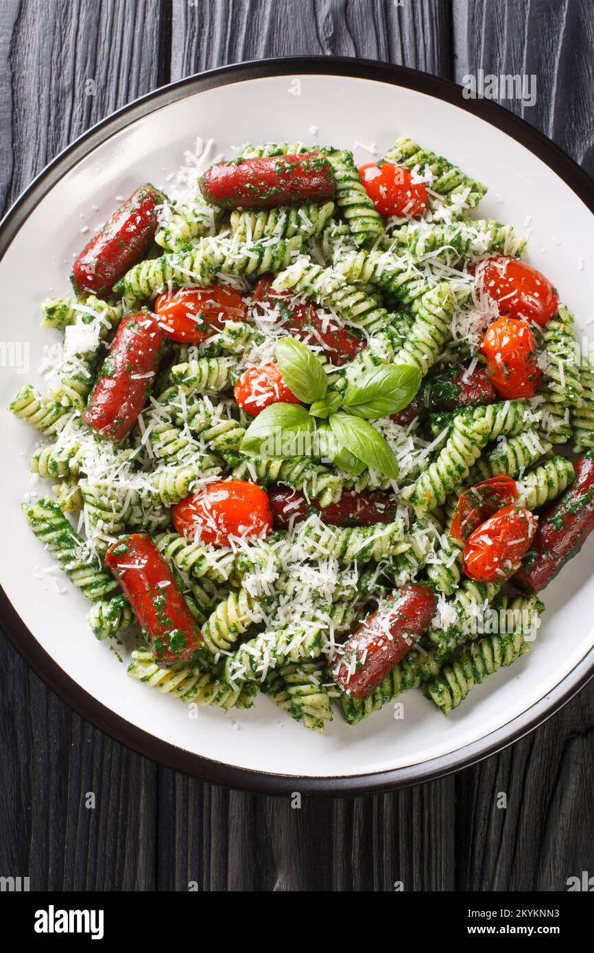 Salsiccia gustosa, pomodoro e Pesto Pasta primo piano sul piatto sul tavolo. Vista verticale dall'alto Foto Stock