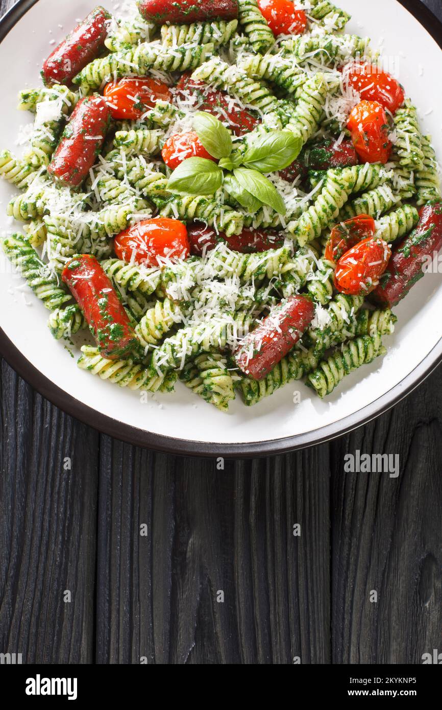 Piatto di pasta sostanzioso con pesto genovese, salsiccia, pomodori e parmigiano primo piano sul piatto della tavola. Vista verticale dall'alto Foto Stock