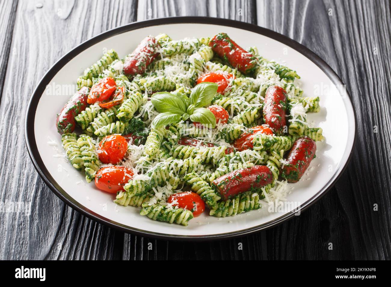Salsiccia di Pesto verde Pasta con pomodori e parmigiano primo piano sul piatto della tavola. Orizzontale Foto Stock
