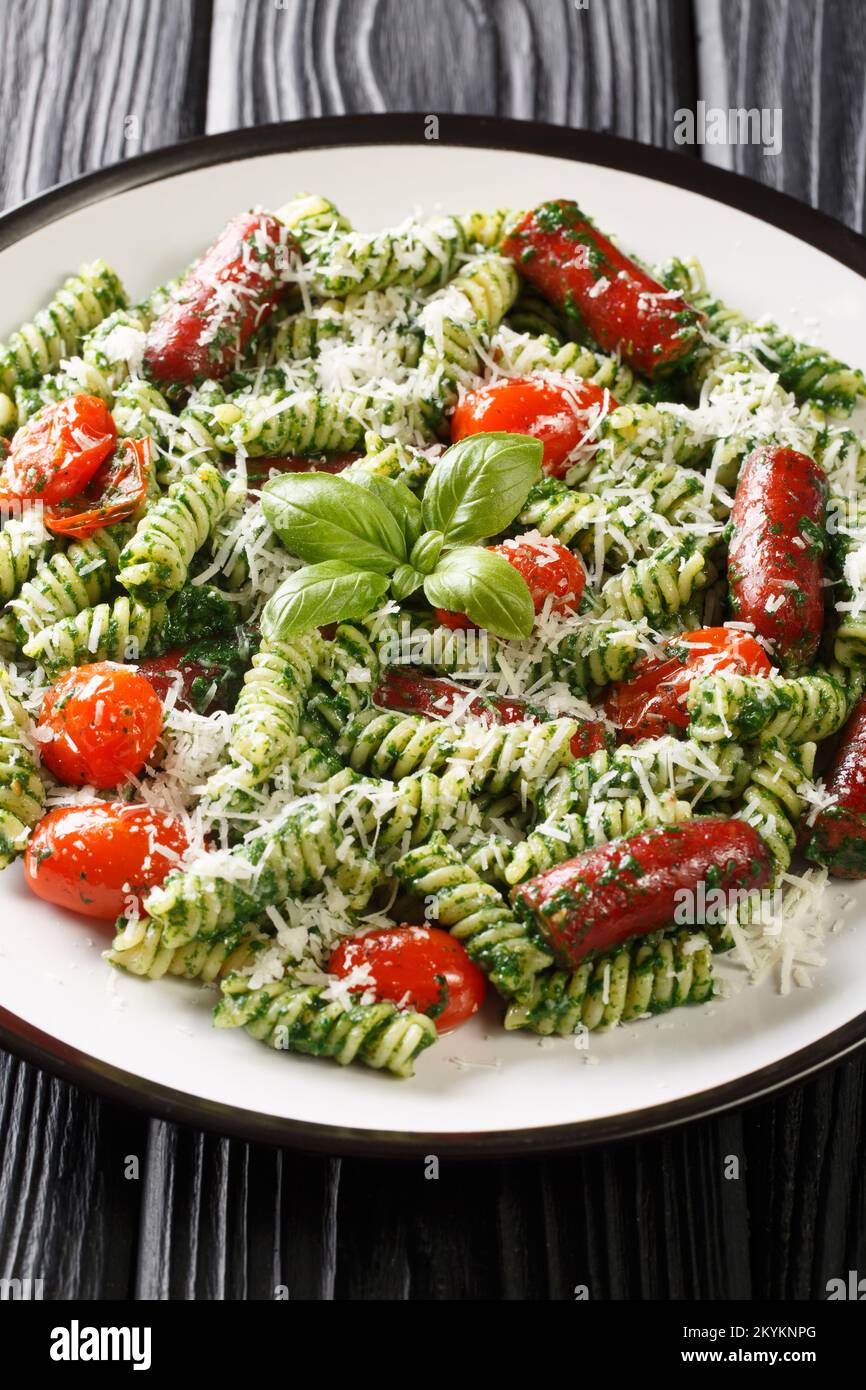 Salsiccia gustosa, pomodoro e Pesto Pasta primo piano sul piatto sul tavolo. Verticale Foto Stock