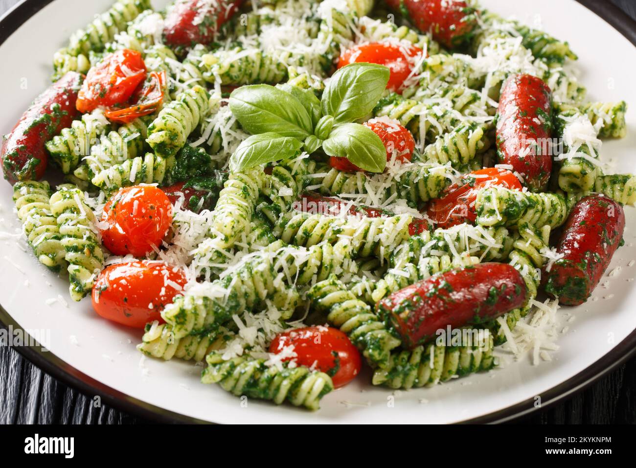 Insalata italiana di fusilli con salsicce, pomodori, pesto e parmigiano primo piano in un piatto sul tavolo. Orizzontale Foto Stock