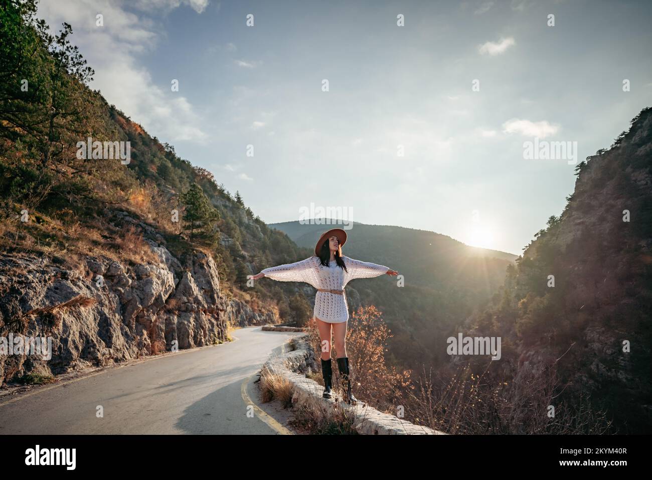 Donna viaggiatore in cappello marrone e maglione bianco che guarda le montagne e la foresta incredibili, il concetto di viaggio wanderlust, momento epico atmosferico Foto Stock