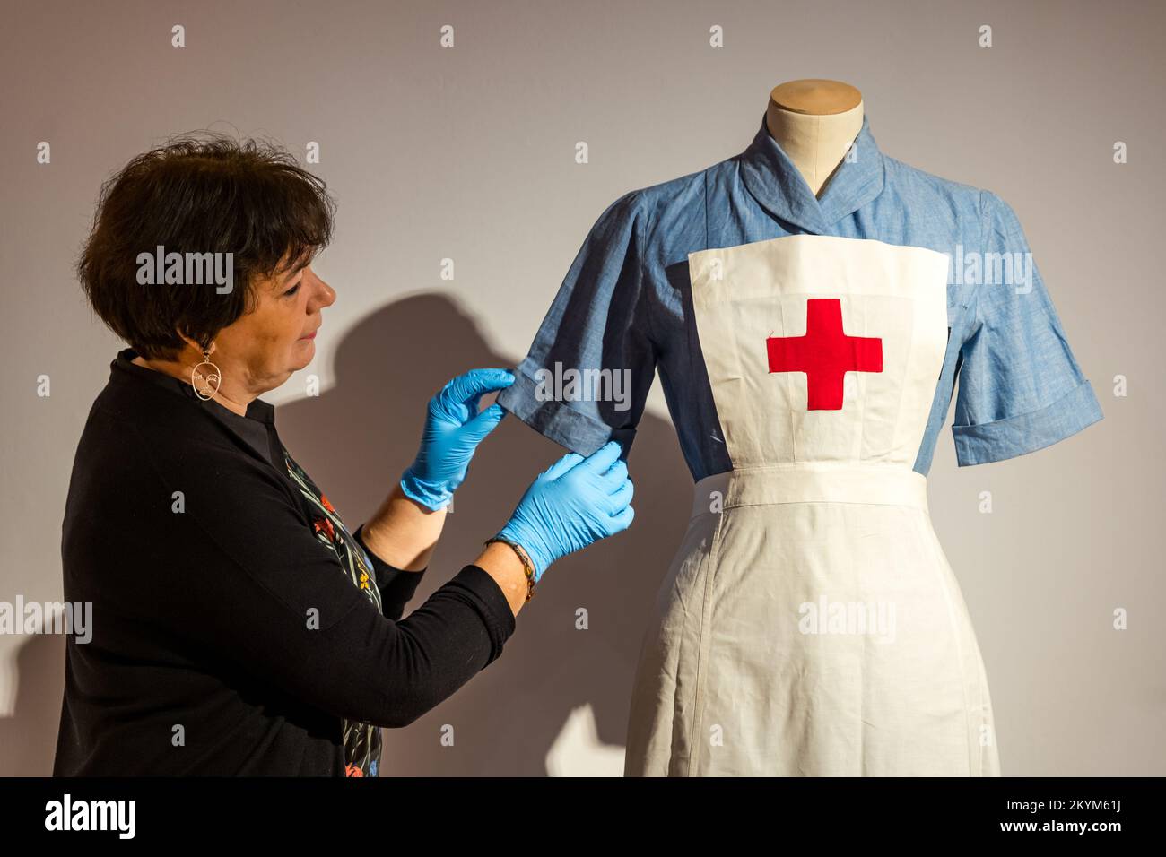 City Art Centre, Edimburgo, Scozia, Regno Unito, 01 dicembre 2022. Auld Reekie mostra di rielaborazione: Si rifanno i ritocchi alla mostra della galleria, culmine del più grande progetto di inventario delle collezioni mai intrapreso nella storia del concilio. Auld Reekie Retold collega gli oggetti della collezione che è cresciuta dagli anni '1870s con le persone e i luoghi della città. Nella foto: Una donna ammira un'uniforme da infermiera indossata da Margaret Erskine di Edimburgo che lavorava nel distaccamento volontario di aiuto durante la seconda guerra mondiale Credit: Sally Anderson/Alamy Live News Foto Stock