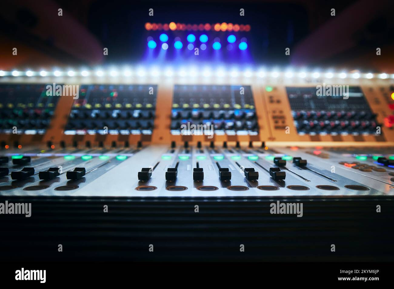 Messa a fuoco selettiva sui cursori della console di mixaggio audio professionale contro i faretti colorati. Foto Stock