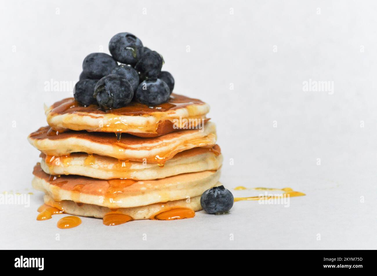 Una pila di frittelle isolate su uno sfondo bianco con mirtilli freschi e sciroppo Foto Stock
