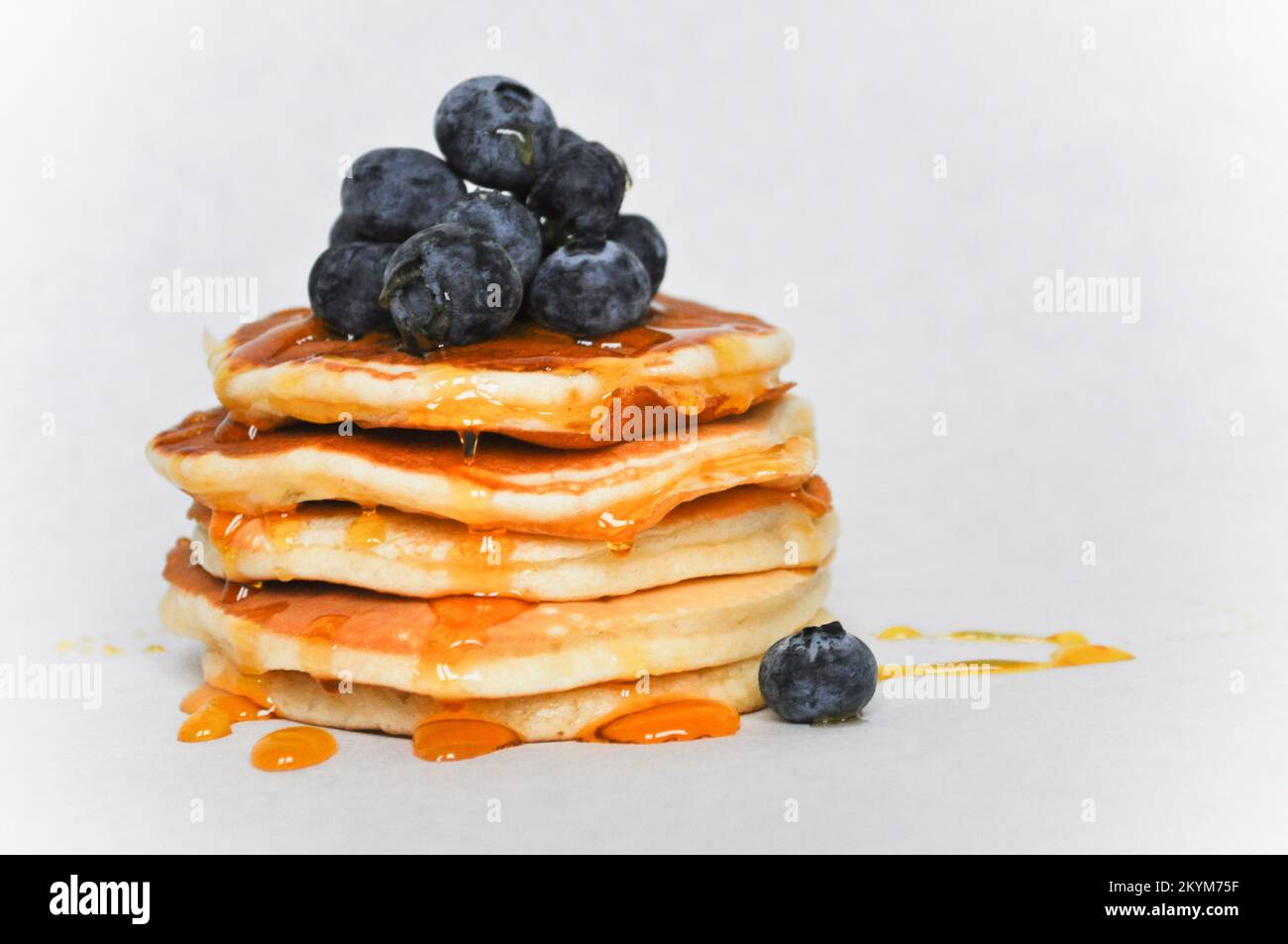 Una pila di frittelle isolate su uno sfondo bianco con mirtilli freschi e sciroppo Foto Stock