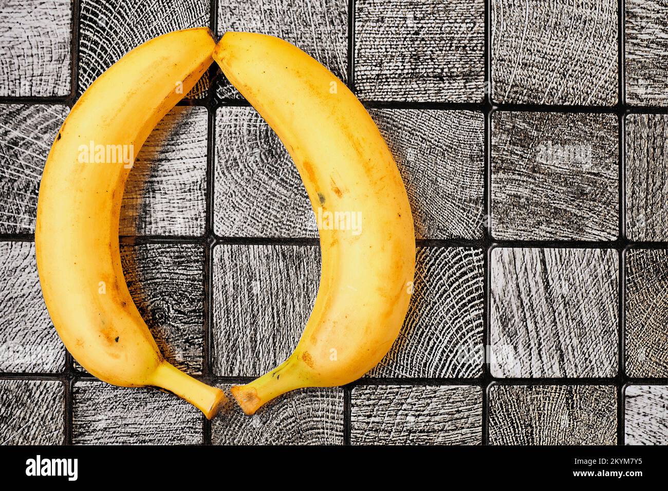 Due banane gialle mature su una superficie grigia piastrellata a scacchi. Spazio per il testo Foto Stock