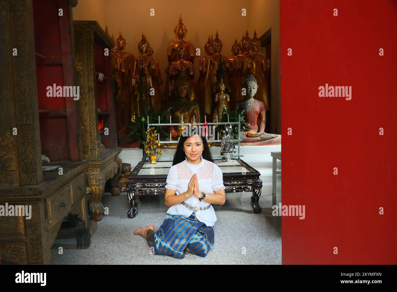 Una signora thailandese in costume thailandese sorride e mette le mani insieme in saluto nella sala di ordinazione buddista Foto Stock