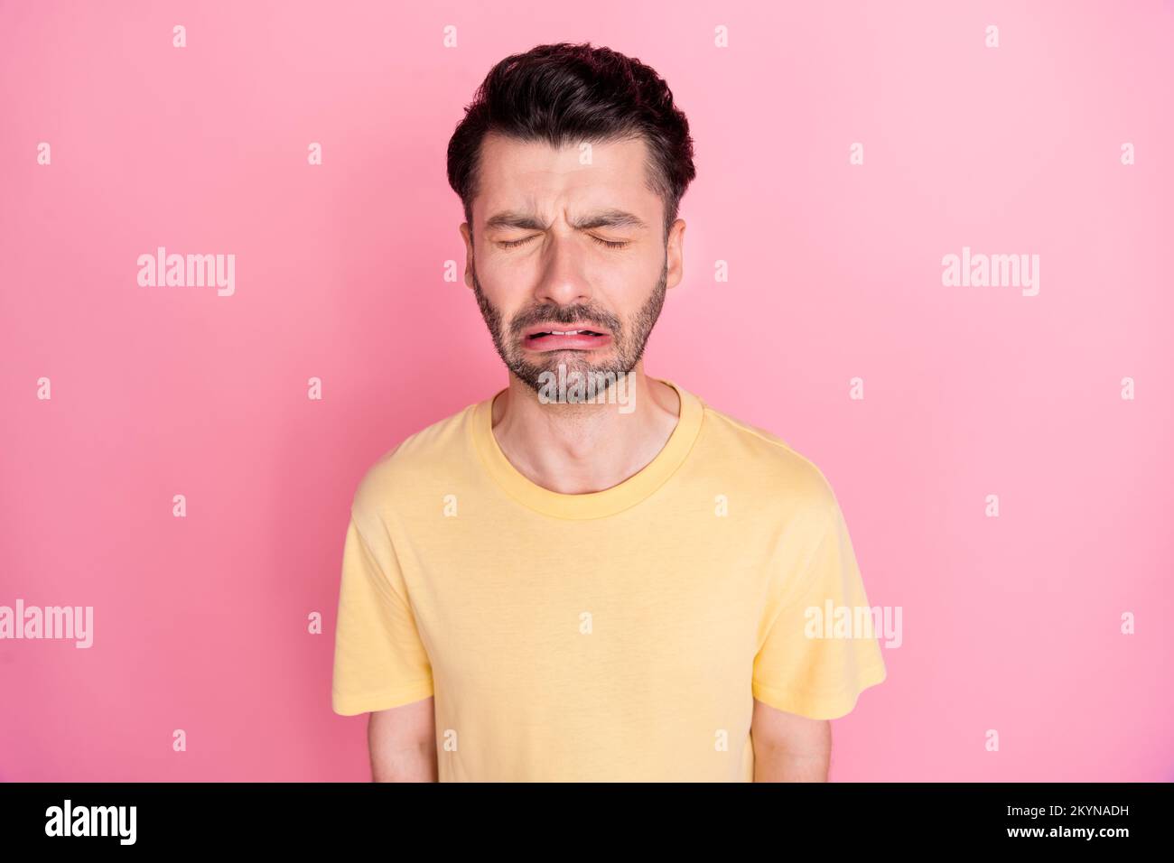 Foto di deluso depresso ragazzo infelice con brunetto acconciatura giallo t-shirt piangendo gli occhi chiusi isolato su sfondo di colore rosa Foto Stock