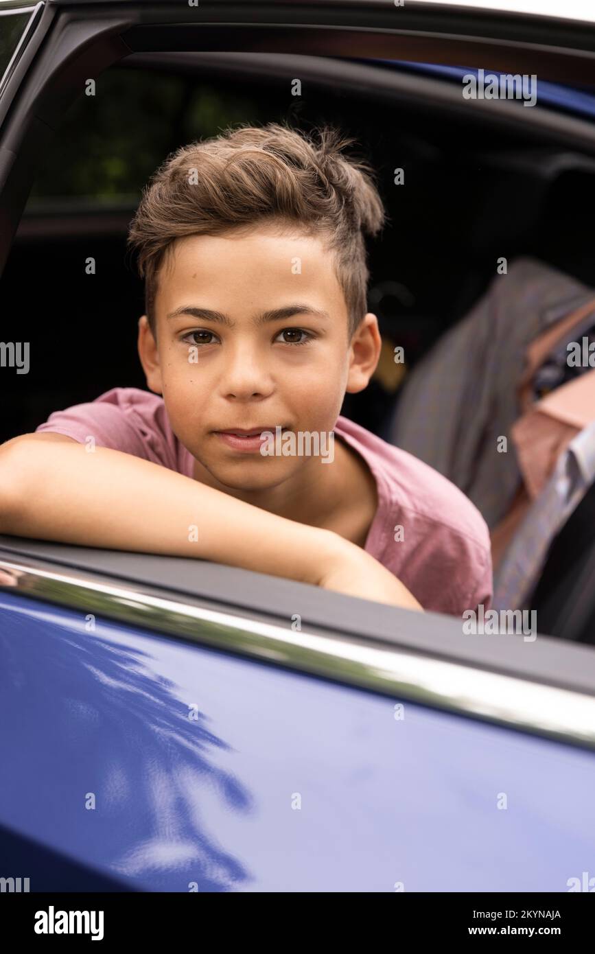 Ritratto del ragazzo appoggiato sulla porta dell'auto visto attraverso la finestra Foto Stock