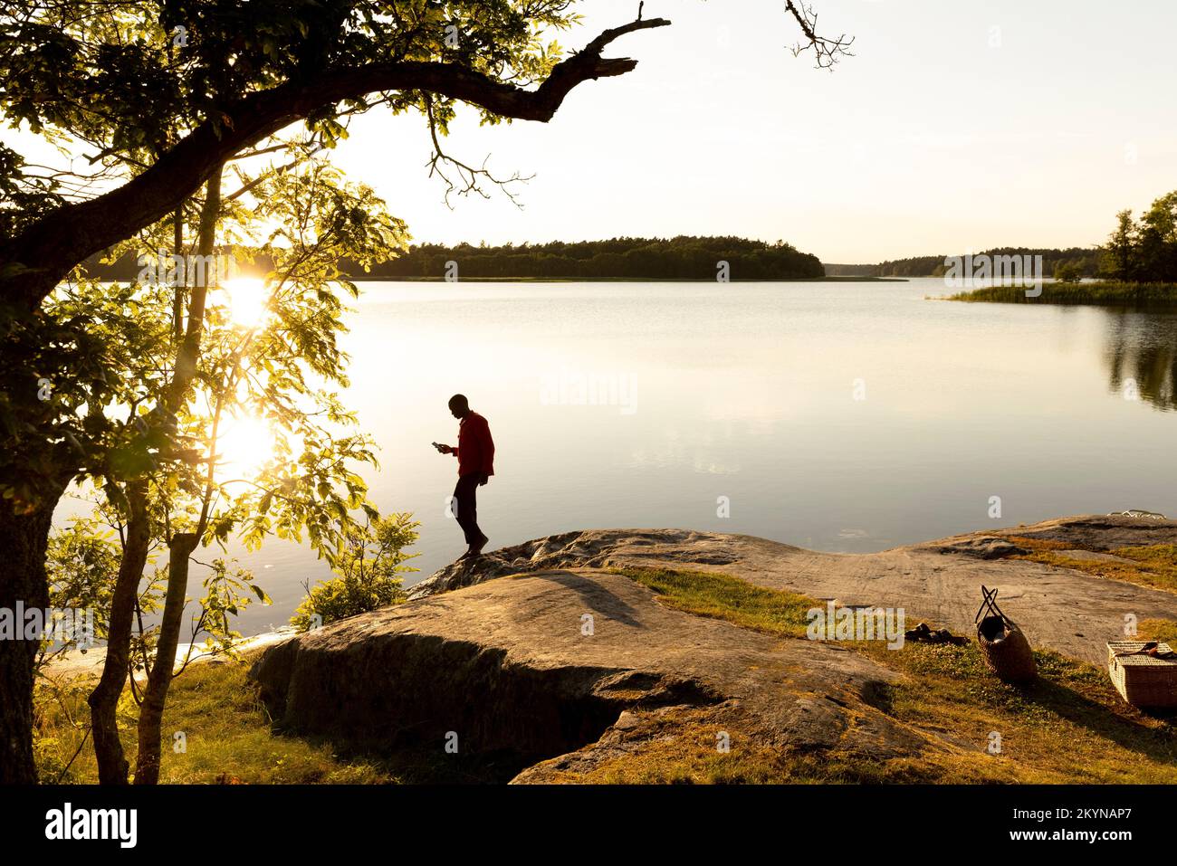 Vista laterale dell'uomo in piedi sulla roccia al lago durante il tramonto Foto Stock