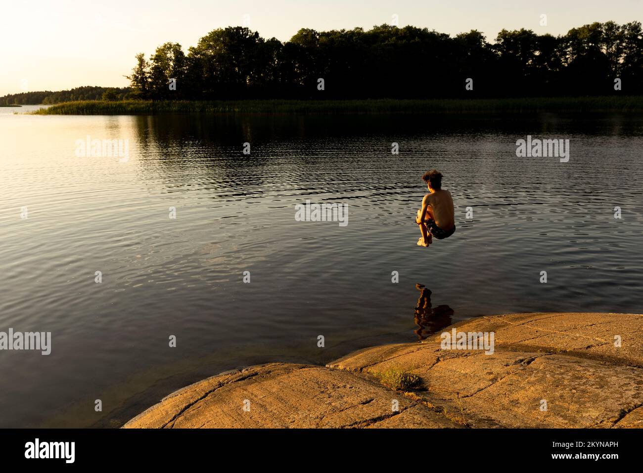 Ragazzo che salta nel lago durante le vacanze al tramonto Foto Stock