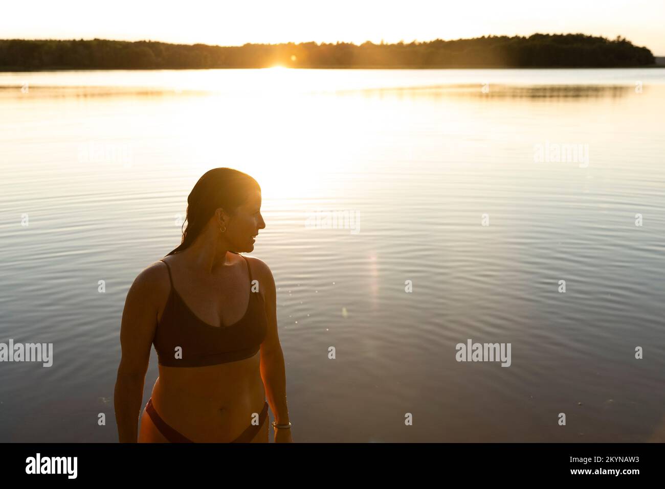 Donna in bikini che guarda lontano mentre si trova contro il lago durante le vacanze Foto Stock