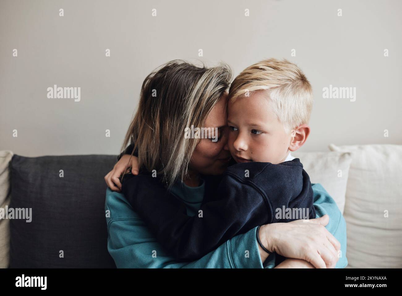 Madre abbraccia il figlio mentre si siede sul divano a casa Foto Stock