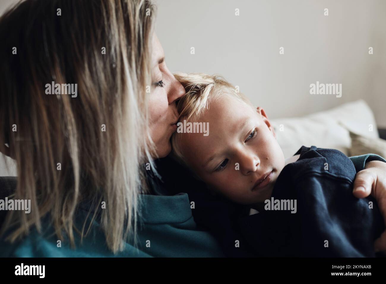 Madre bacia il figlio seduto sul divano a casa Foto Stock