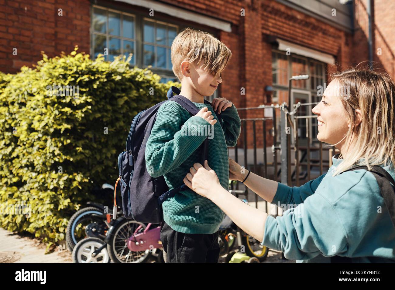Madre felice che guarda il figlio con lo zaino fuori dalla scuola Foto Stock