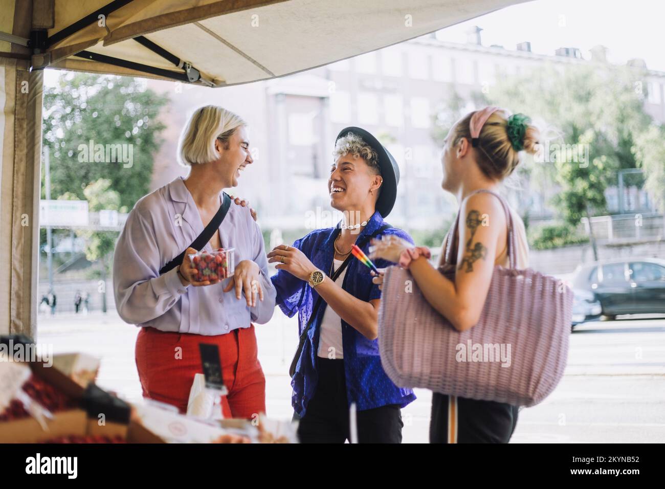 Felice giovane uomo che parla con un amico non binario che tiene un contenitore di frutta Foto Stock