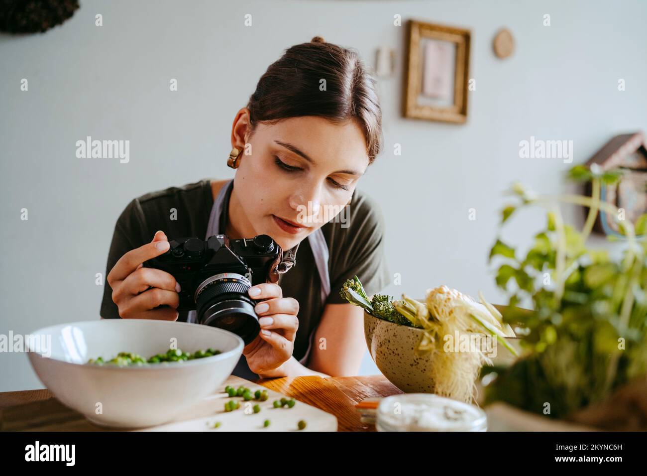 Stilista di alimentari che regola l'obiettivo della fotocamera mentre fotografa i piselli verdi in studio Foto Stock