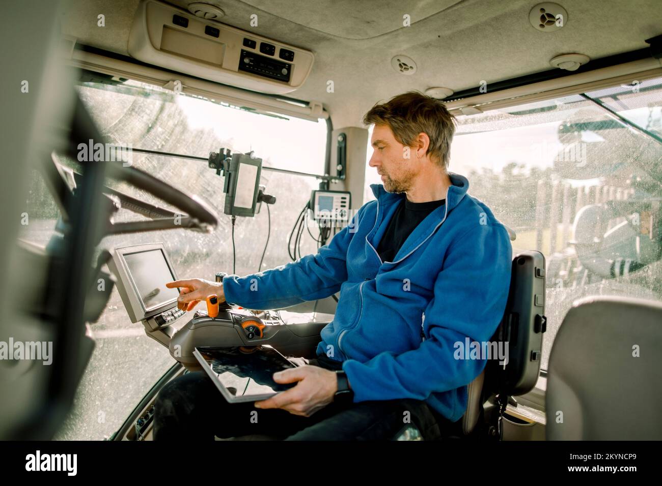 Il contadino che utilizza il computer seduto nel trattore in azienda Foto Stock