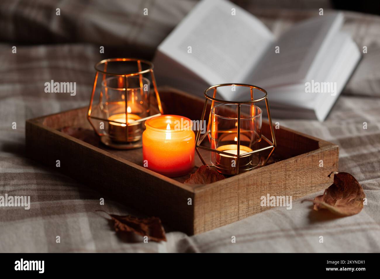 calda camera accogliente inverno o autunno concetto, candele su vassoio e un libro Foto Stock