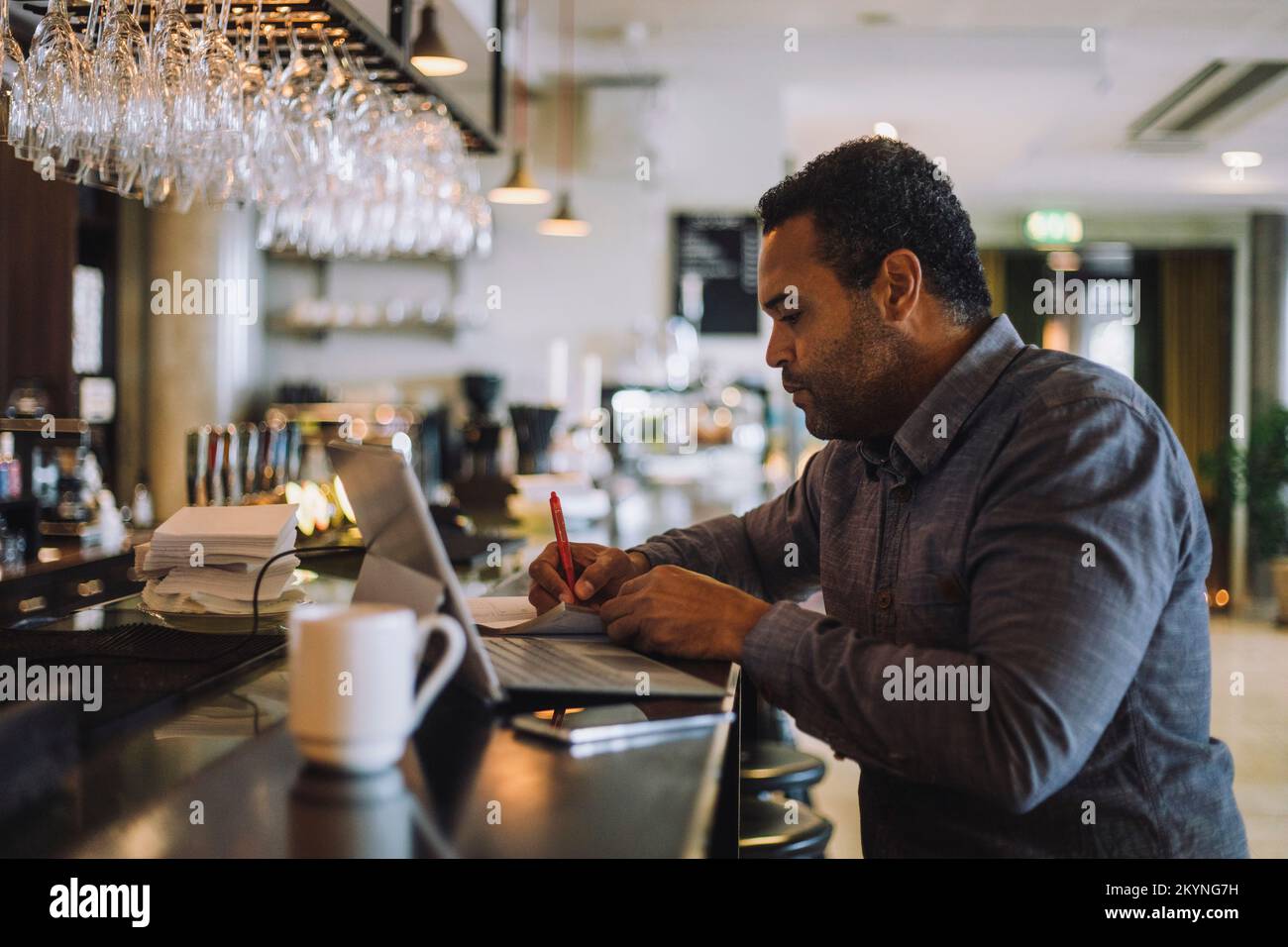 Un uomo d'affari scrive mentre si siede con un computer portatile al banco del bar Foto Stock Un uomo d'affari scrive mentre si siede con un computer portatile al banco del bar Foto Stock