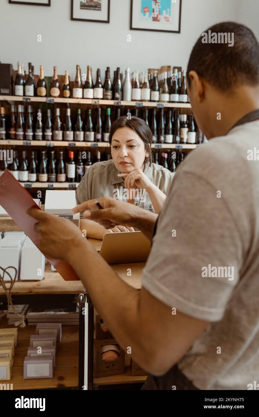 Proprietario maschio che mostra l'inventario a una collega femmina al negozio di vini Foto Stock