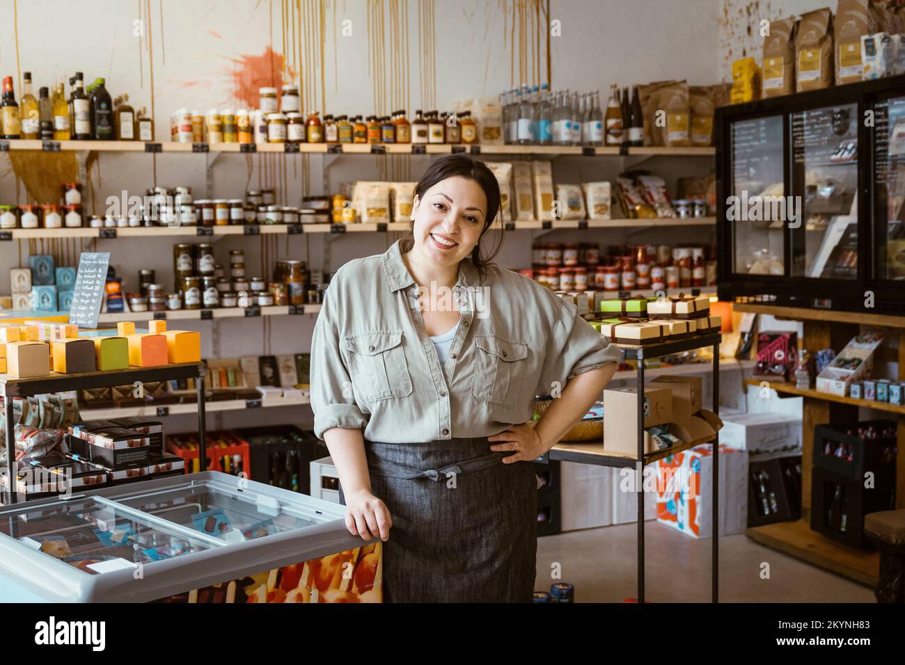 Ritratto di donna titolare con mano sul fianco in piedi presso il congelatore per gelato in negozio Foto Stock