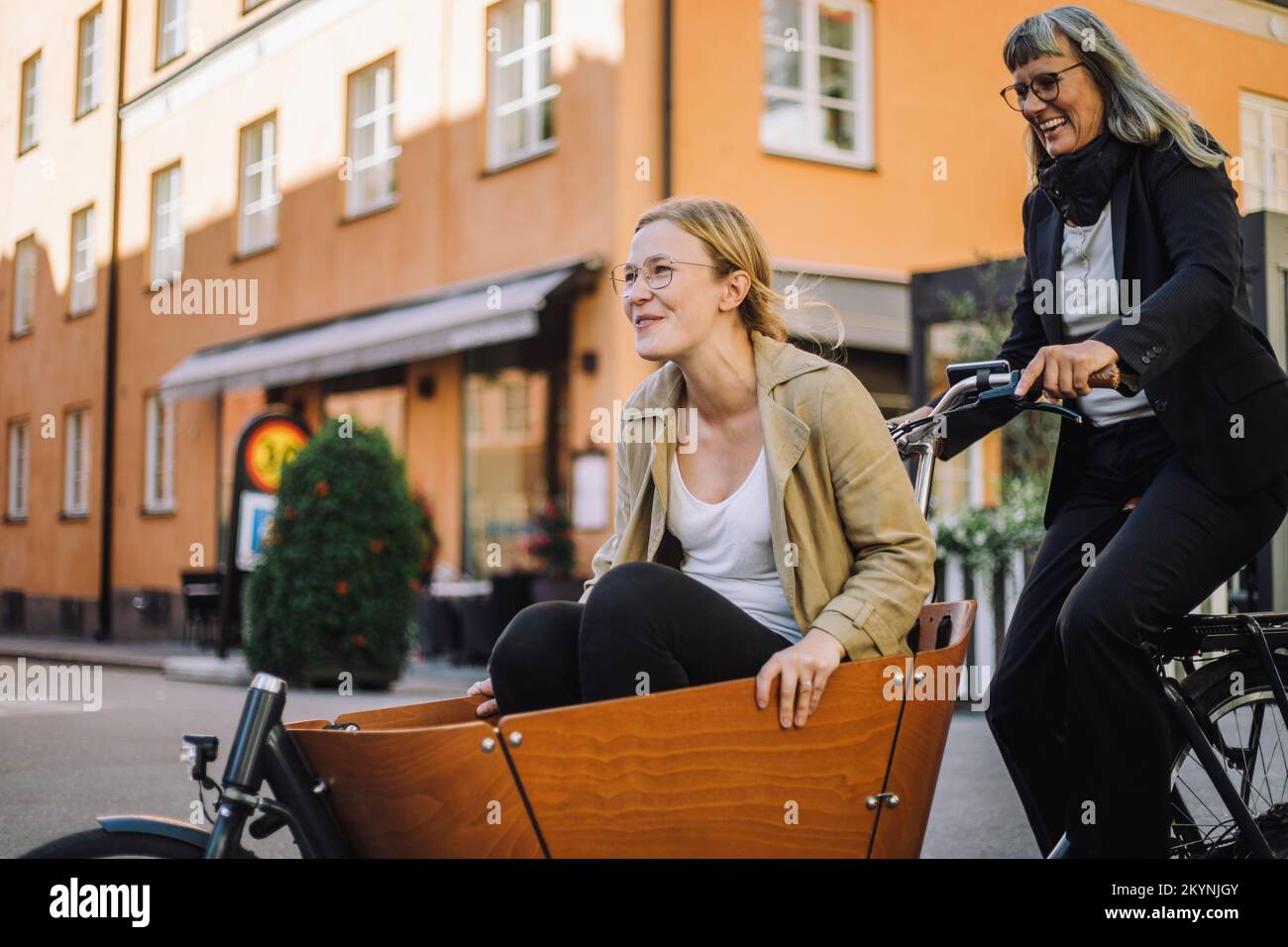Felice donna d'affari matura in bicicletta da carico con una collega in città Foto Stock