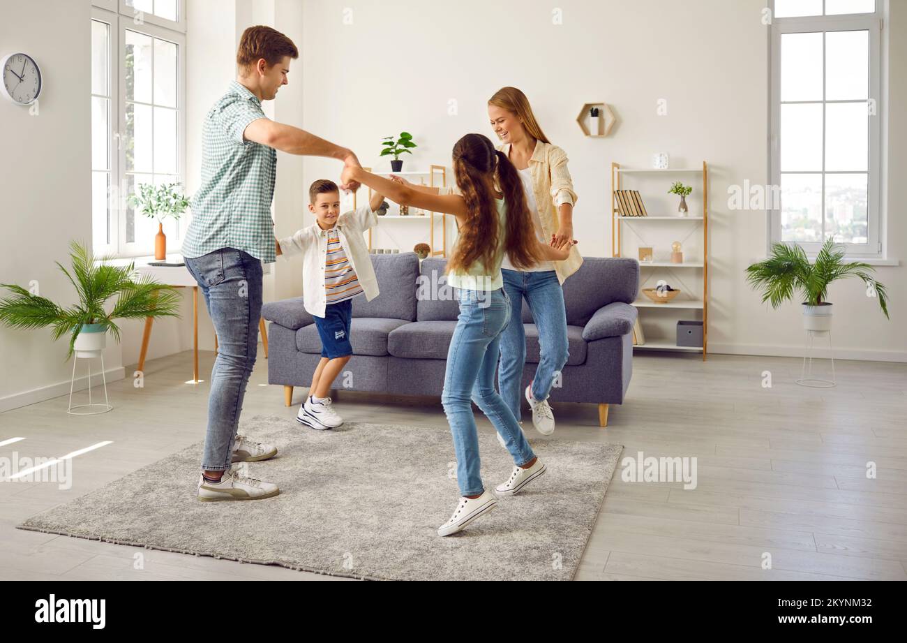 Buon mamma, papà, figlia e figlio di famiglia che giocano a condurre una danza rotonda a casa nel soggiorno. Foto Stock