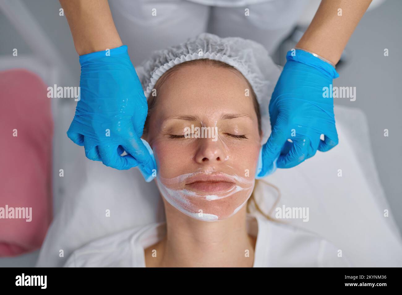 L'estetista lava la faccia della donna usando i tamponi di cotone per rimuovere la maschera facciale Foto Stock