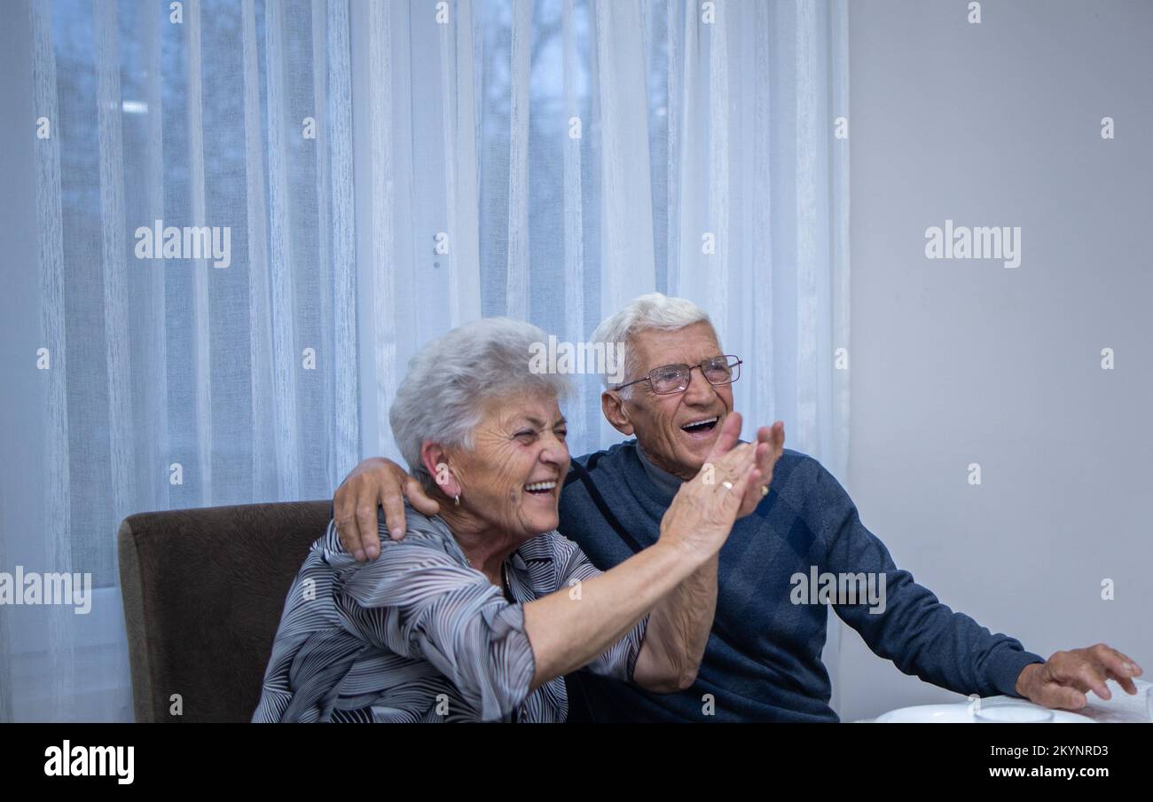 una coppia sposata anziana tra le braccia sorride con orgoglio. un uomo festeggia il suo 80th° compleanno, abbracciando la moglie che applaude e perlude Foto Stock