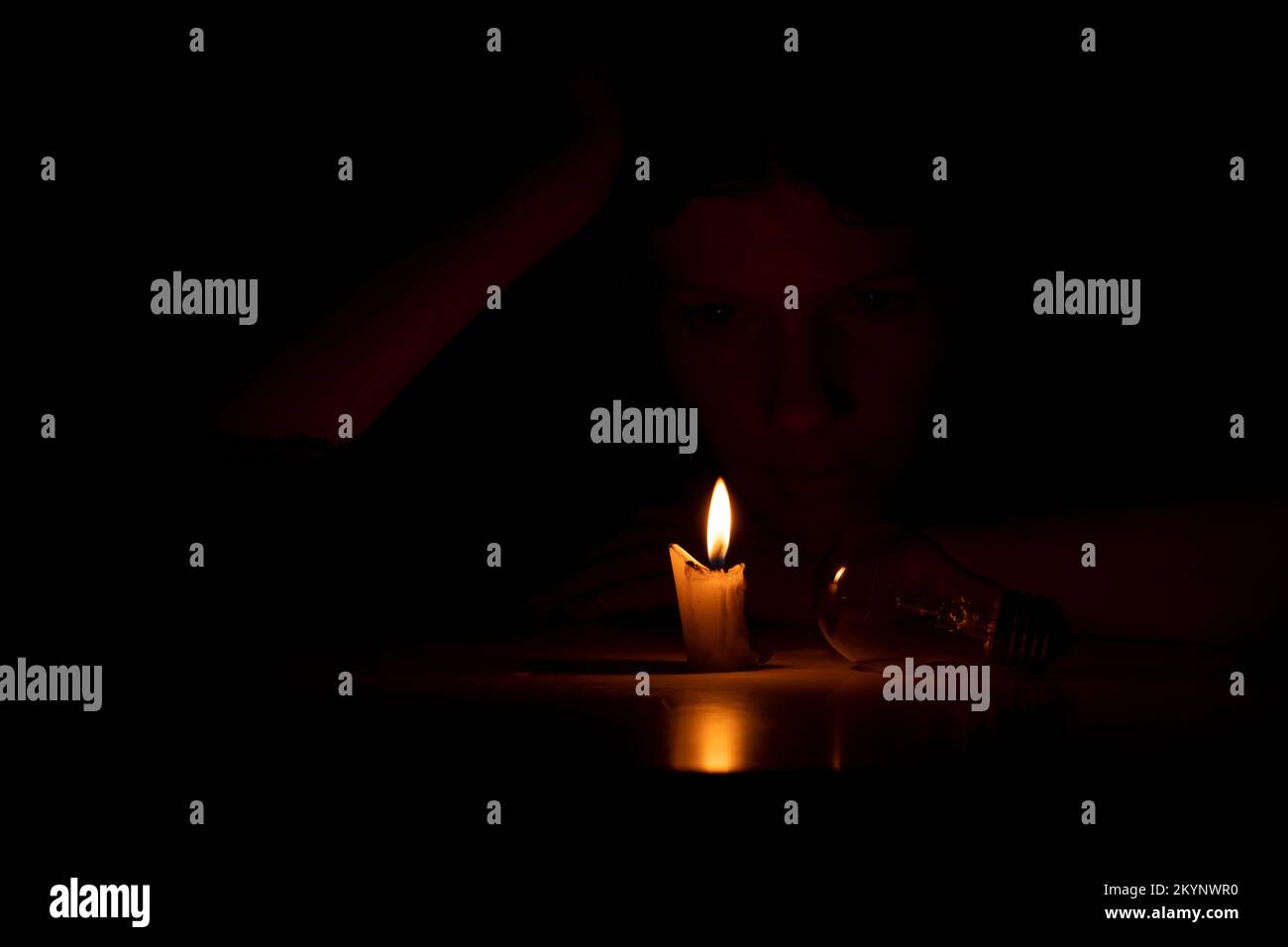Una ragazza al buio si siede con candele e una lampadina a un tavolo al buio a casa, persone senza luce a casa Foto Stock