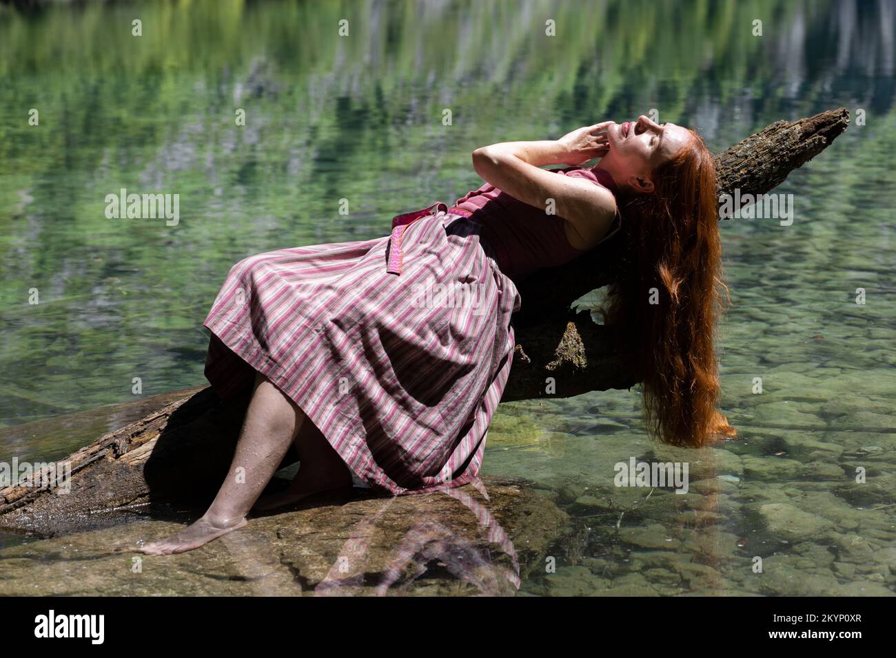 Una giovane donna giace su un tronco vicino ad un lago di montagna di colore smeraldo Foto Stock