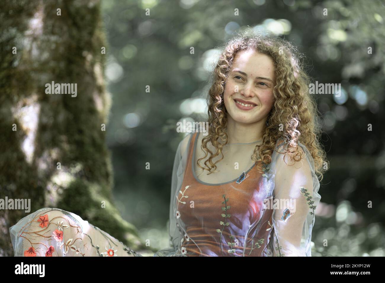 Ritratto di un giovane modello ricci dai capelli lunghi con un sorriso sul volto su uno sfondo di verde Foto Stock