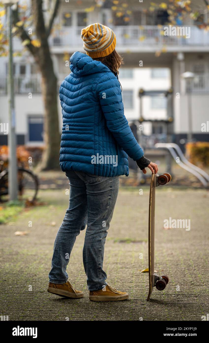 Skater ragazza con un longboard in strada indossando abiti invernali, visto da dietro Foto Stock