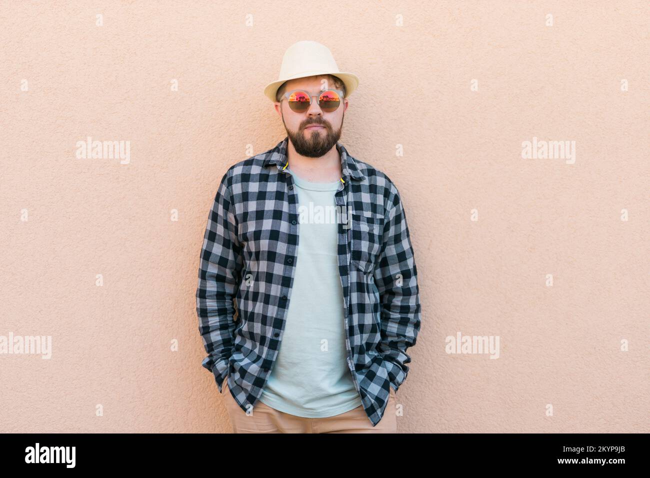 Uomo bearded in abiti estivi e cappello stand su parete beige sulla strada città urbano e concetto di viaggio - copia spazio e spazio vuoto per la pubblicità Foto Stock
