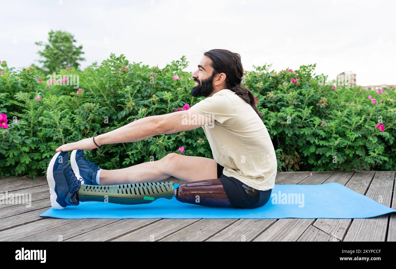 Atleta ispanico con protesi delle gambe che si allunga sul tappetino yoga Foto Stock