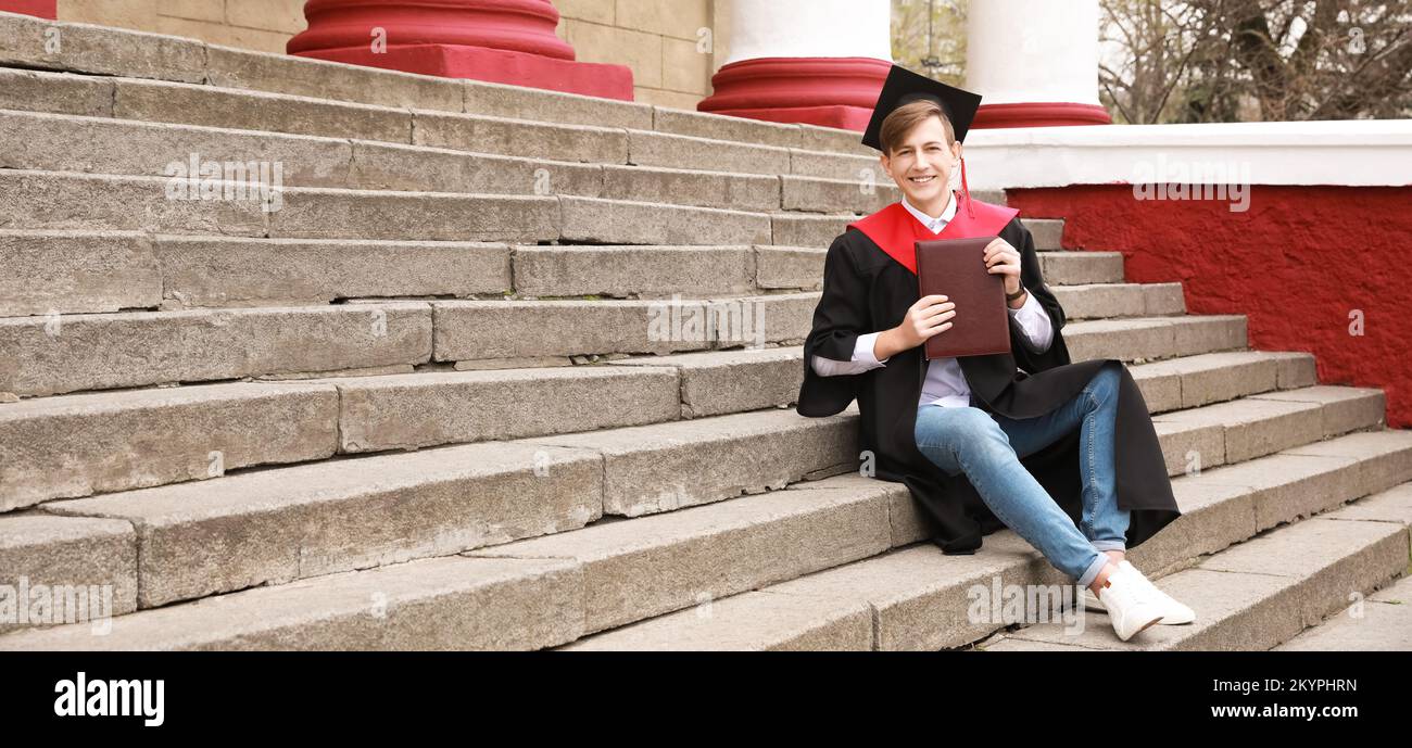 Studente di laurea maschile seduto sulle scale all'aperto Foto Stock