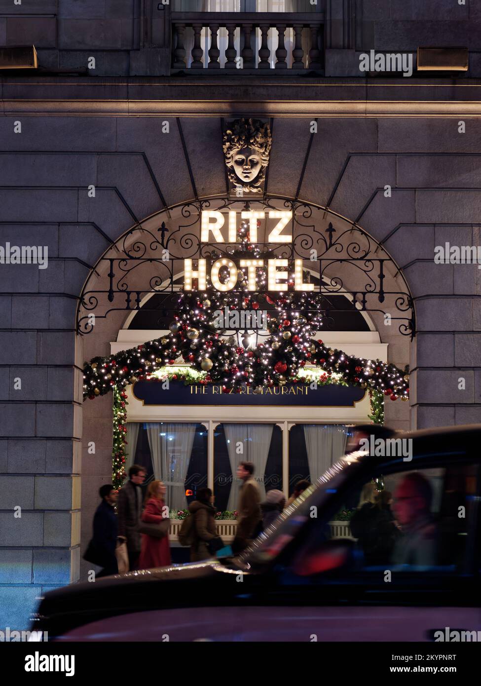 Ritz Hotel Christmas Display. I pedoni camminano e un taxi passa offuscato dal movimento con luci che si riflettono sul parabrezza. Foto Stock