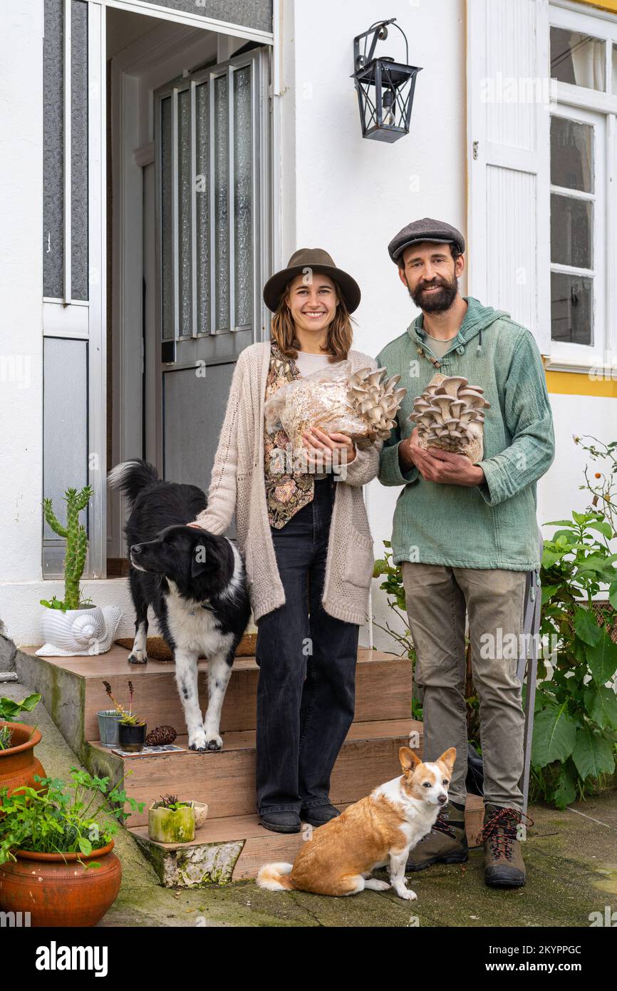 Giovane coppia che tiene blocchi di funghi ostriche vicino casa Foto Stock