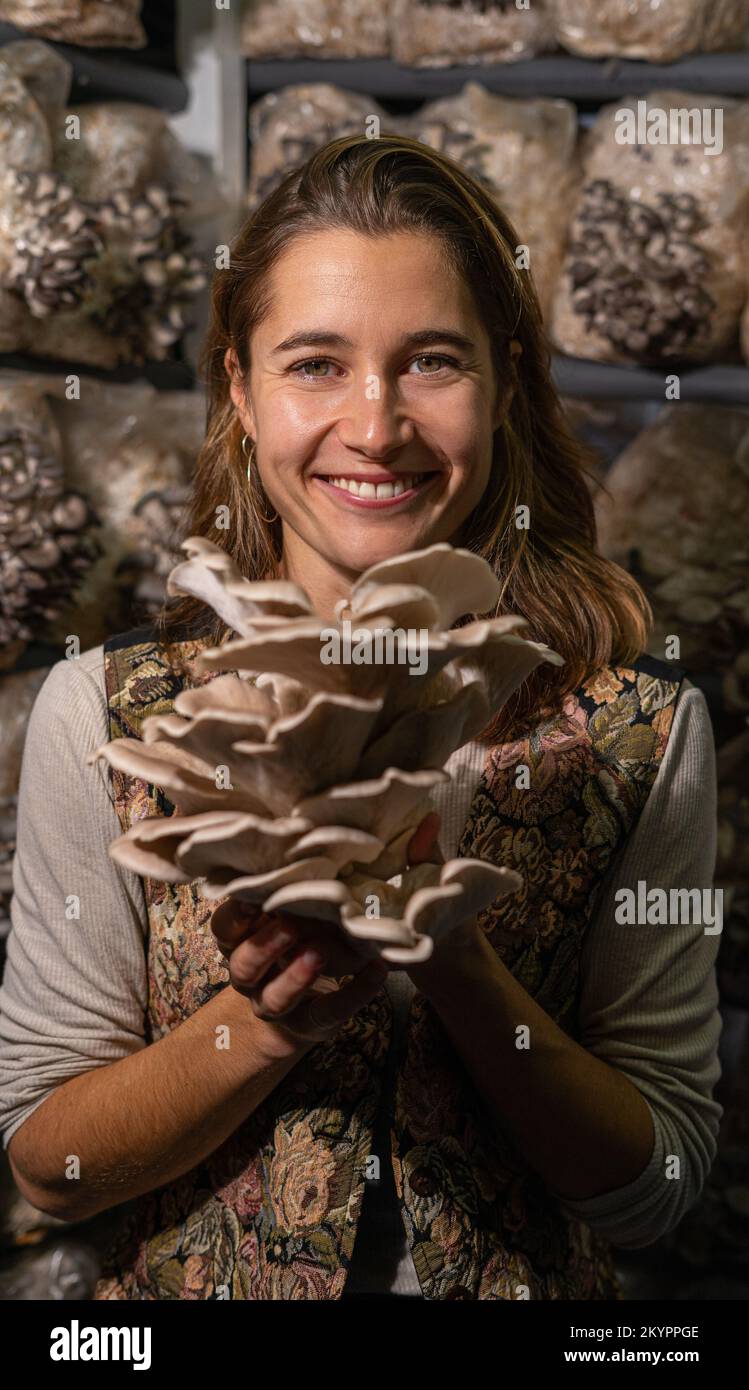 Giovane donna felice che tiene funghi ostriche contro la serra dei funghi. Foto Stock