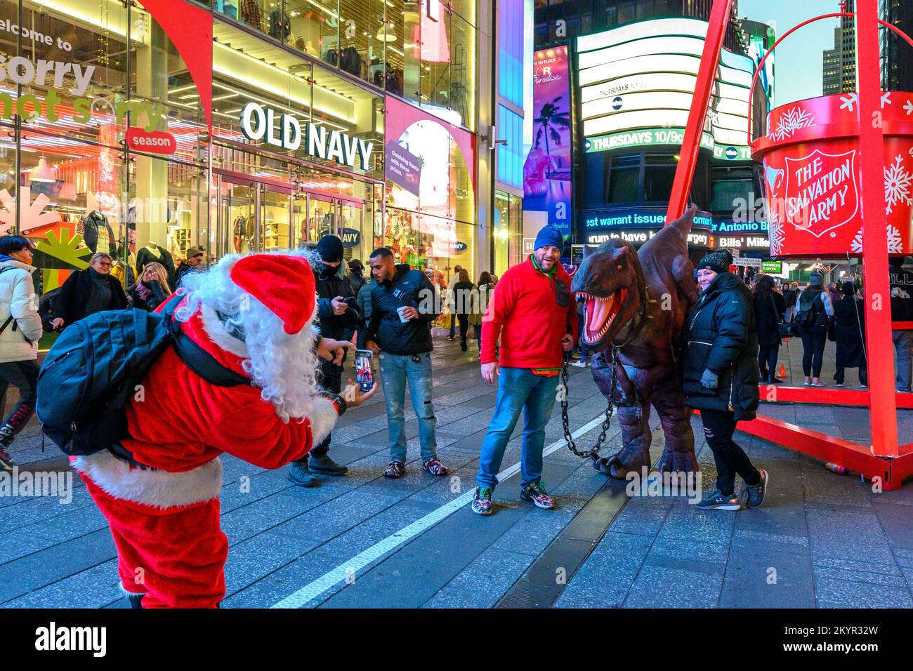 New York, USA, 1 dicembre 2022. Un uomo vestito come Babbo Natale scatta una foto di turisti in posa con un collega su un costume di dinosauro in Times Squar Foto Stock