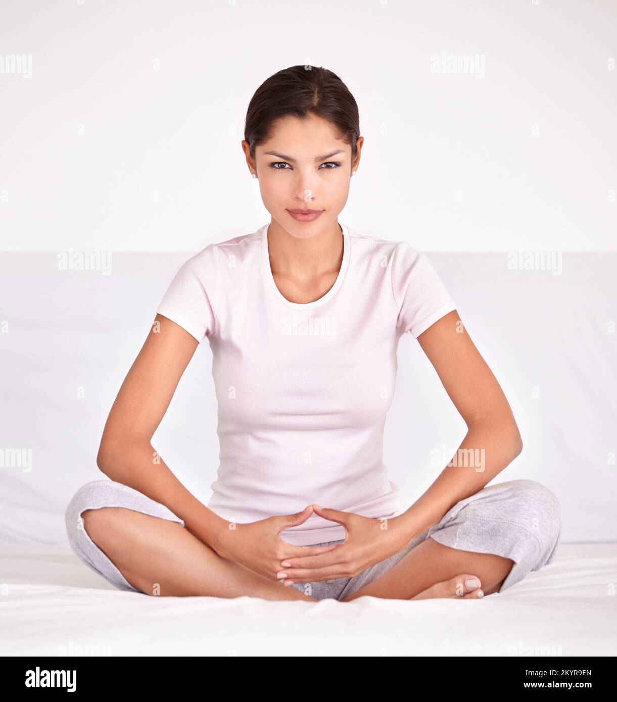Trovare il suo centro spirituale. Una giovane donna seduta a gambe incrociate e meditando. Foto Stock