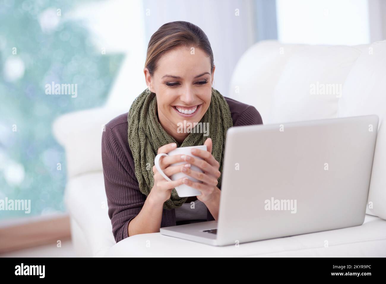 Pausa caffè online. Una giovane donna che tiene una tazza di caffè mentre si trova davanti al suo notebook. Foto Stock