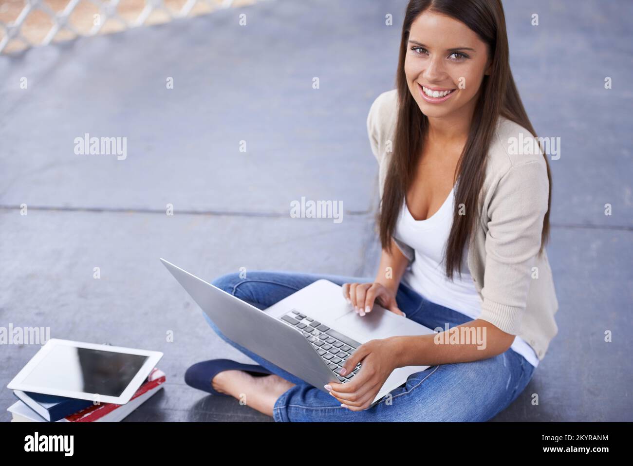 Studia ovunque vada. Un giovane studente seduto all'esterno circondato da libri e che lavora sul suo computer portatile. Foto Stock
