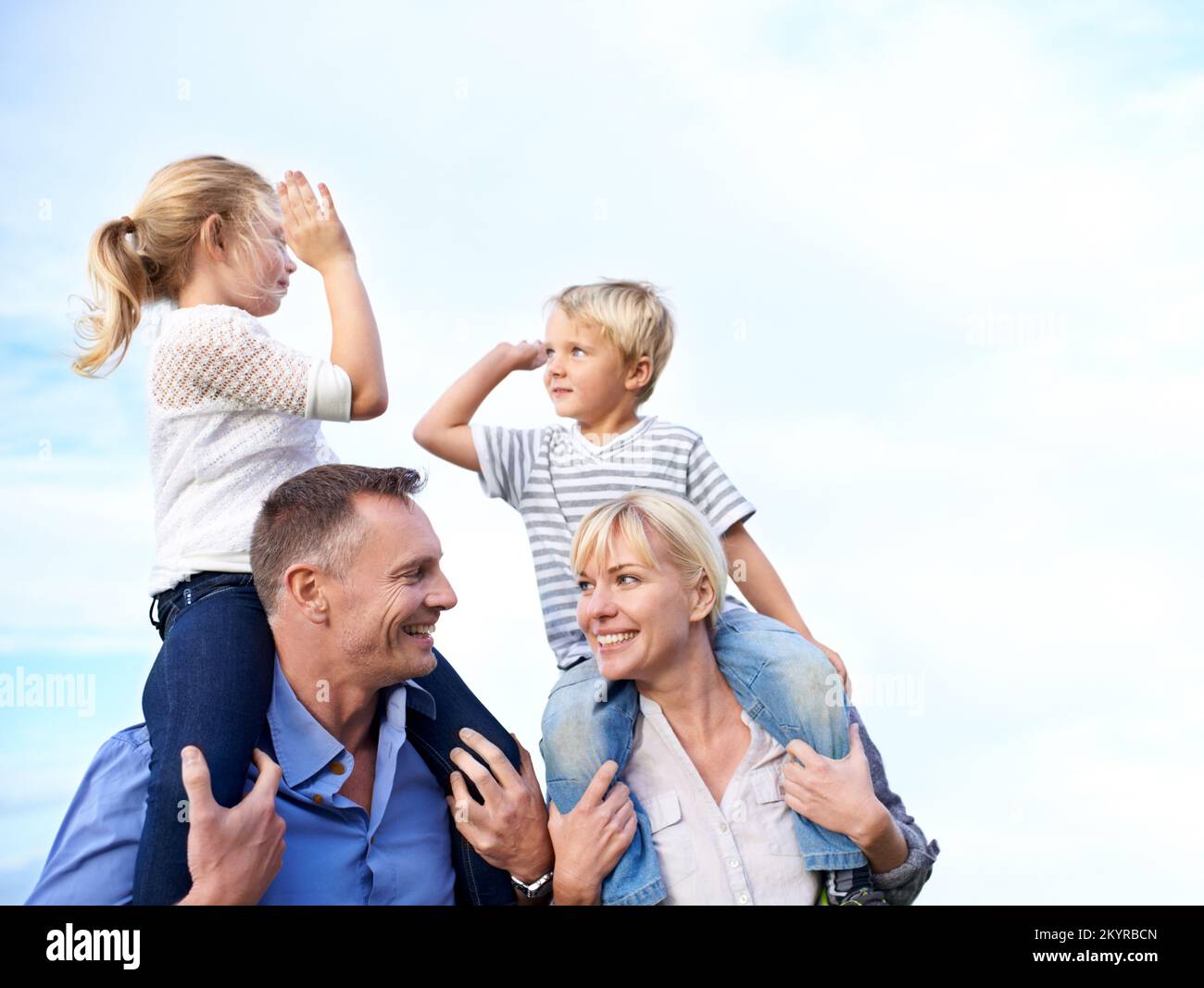 Alto cinque a tempo di famiglia. Vista ritagliata di due genitori che trasportano i loro bambini sulle spalle all'aperto. Foto Stock